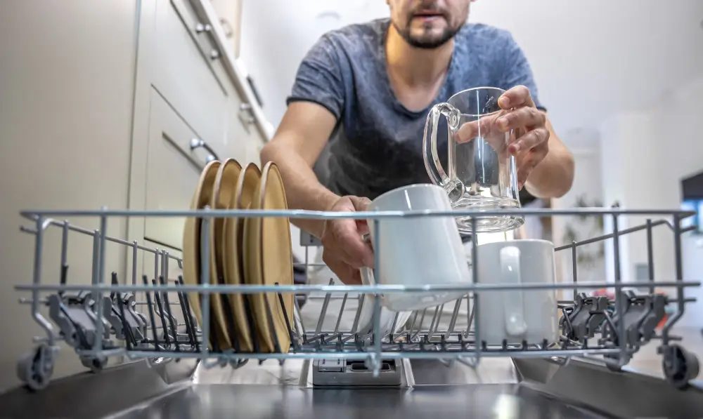 Man putting plates and cups into dishwasher